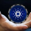 Hand holding Cardano ADA coin showing cryptocurrency logo