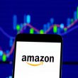 Amazon logo on smartphone with stock market chart showing price movements in background