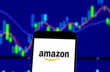 Amazon logo on smartphone with stock market chart showing price movements in background