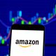 Amazon logo on smartphone with stock market chart showing price movements in background