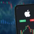 Smartphone displaying Apple logo with stock chart and buy/sell buttons