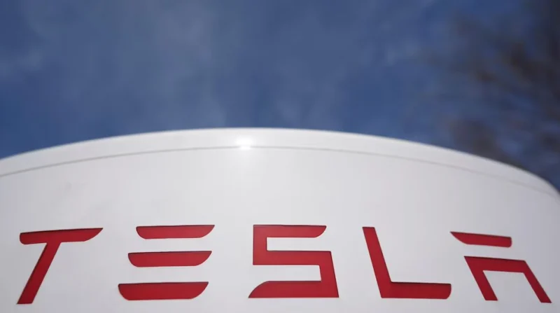 Close-up of red Tesla logo on a white curved surface against a blue sky background