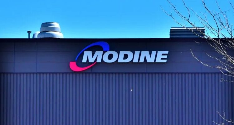 Modine Manufacturing Company logo displayed on the exterior of a dark blue industrial building, featuring the company name in white letters with blue and red swoosh design elements