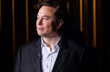 Elon Musk in formal attire against dark background